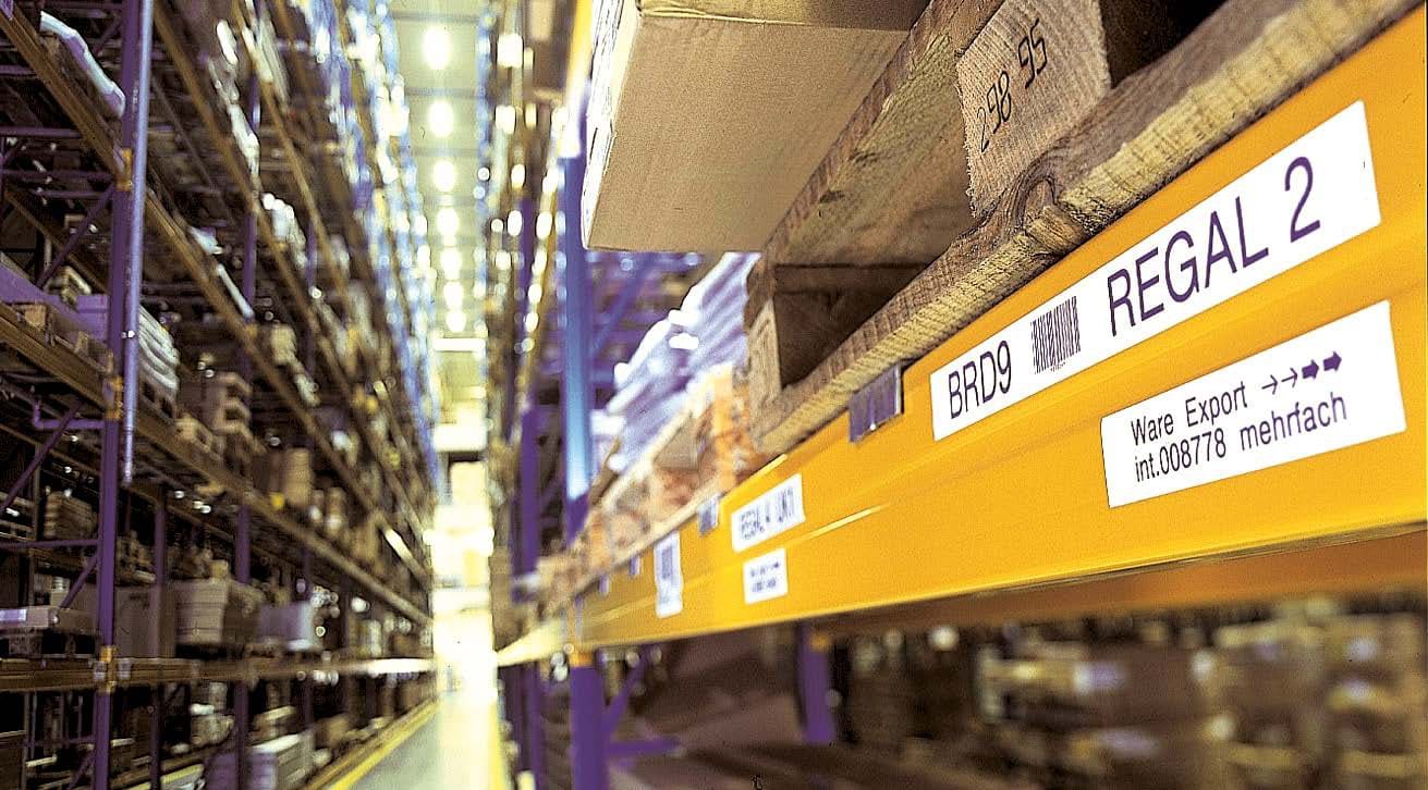 Băng nhãn Brother TZe được dán lên kệ hàng trong một nhà kho, minh họa tính ứng dụng và độ bền